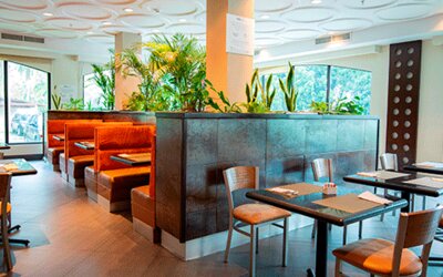 Hotel dining area with tables, chairs, orange booth seating and tropical plants beside large windows at Holiday Inn Panama Canal.