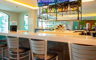 Hotel bar with a white counter, high stools, liquor display and televisions at Holiday Inn Panama Canal.