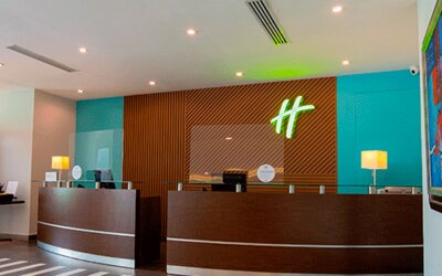 Hotel reception desk with modern wood paneling, teal walls and Holiday Inn branding at Holiday Inn Panama Canal.