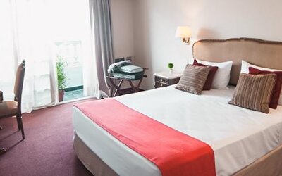 Guest room with a double bed, white linens, red bed runner, desk and balcony doors at Ramada by Wyndham Buenos Aires Centro.