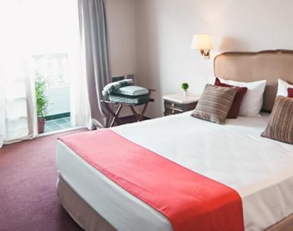 Guest room with a double bed, white linens, red bed runner, desk and balcony doors at Ramada by Wyndham Buenos Aires Centro.