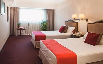 Guest room with two twin beds, white linens, red bed runners, red accent pillows and a large window at Ramada by Wyndham Buenos Aires Centro.