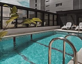 Outdoor swimming pool with turquoise water, metal handrails and white lounge chairs at Ramada by Wyndham Buenos Aires Centro.