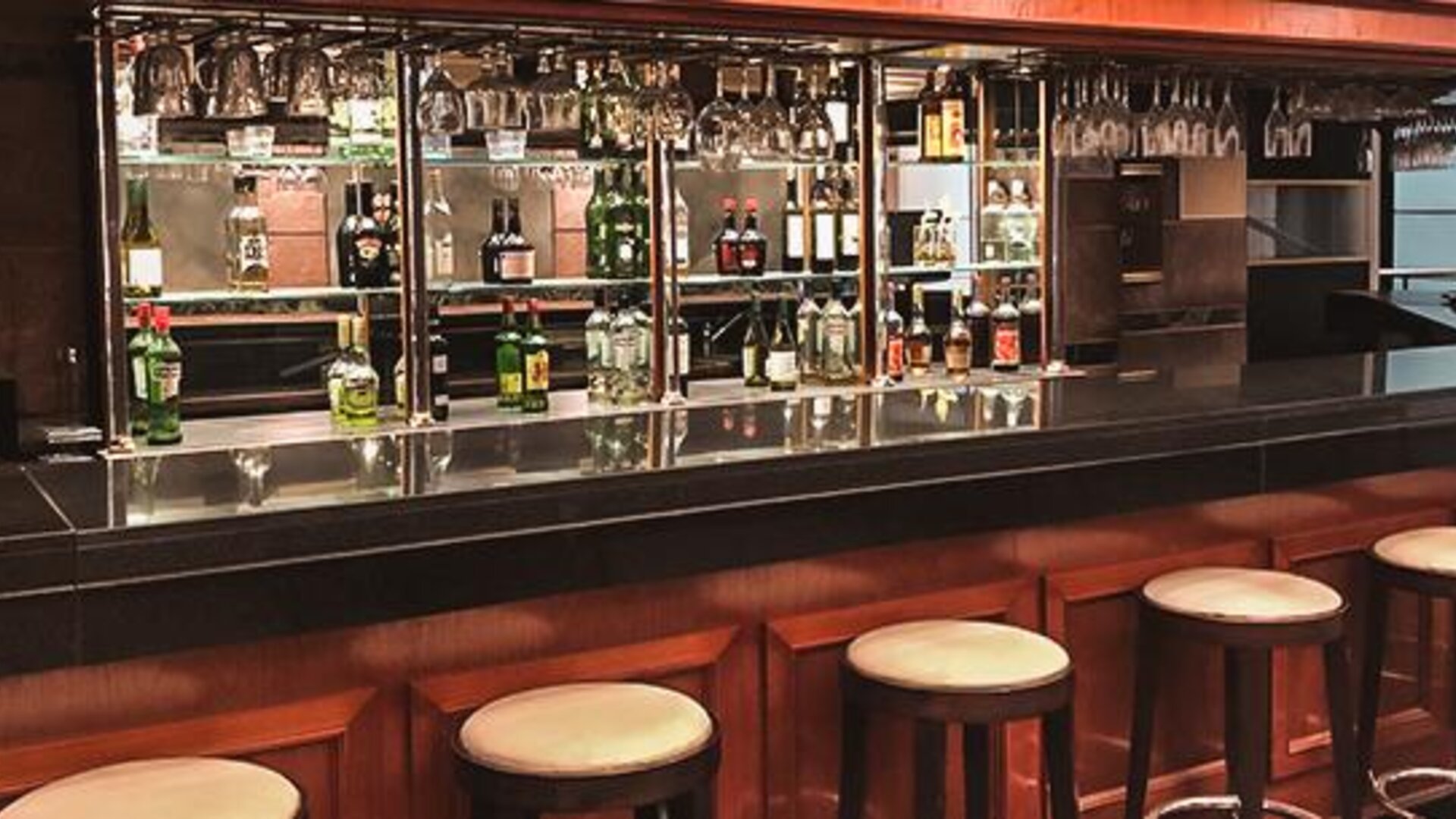 Hotel bar with a dark wood counter, stools, liquor bottles and hanging glassware at Ramada by Wyndham Buenos Aires Centro.