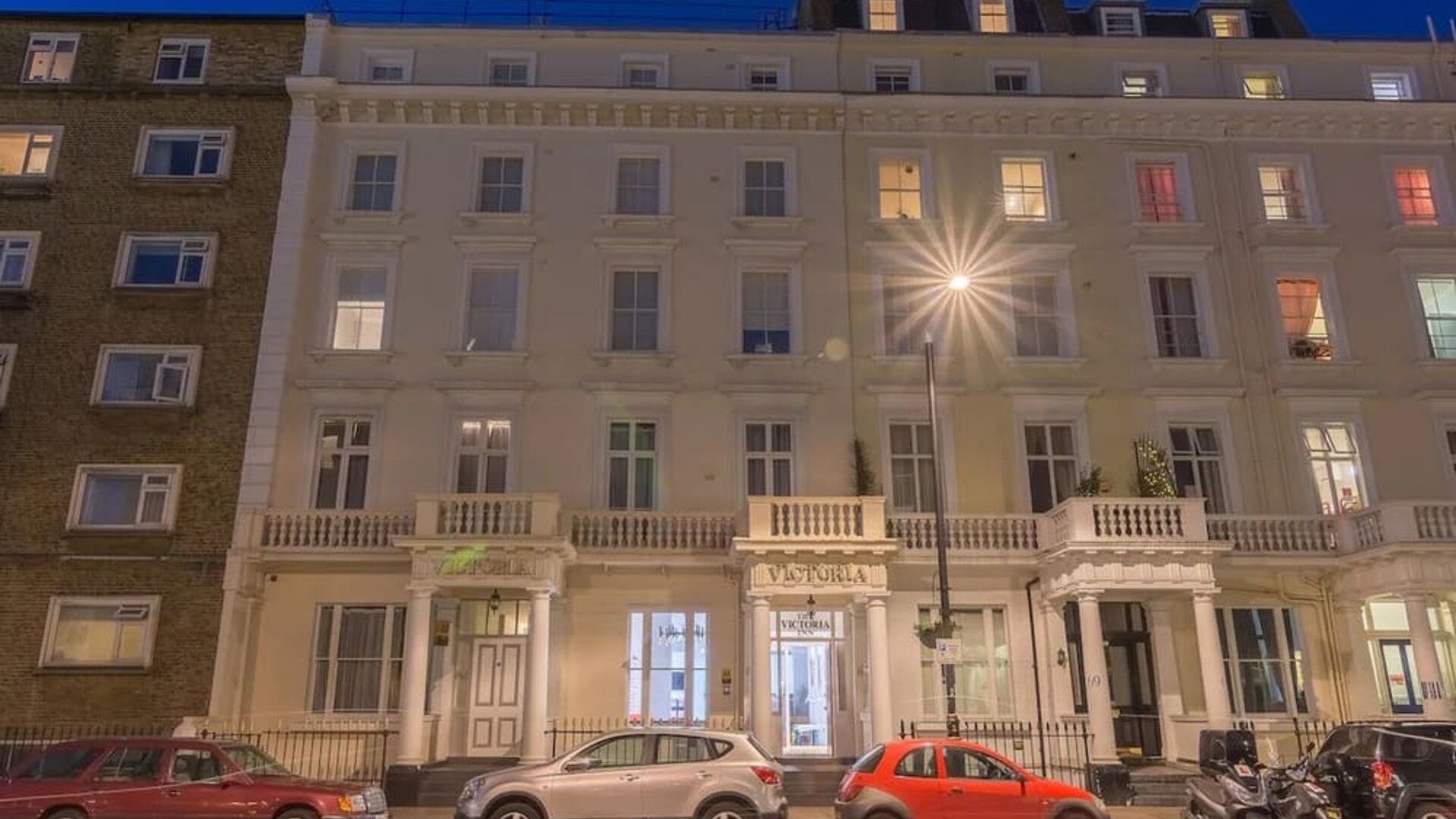 Exterior of Victoria Inn, a white multi-story Victorian-style building with decorative columns and balconies, photographed at night.