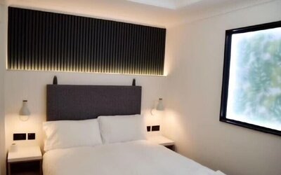 Double guest room with a white bed, dark upholstered headboard, bedside tables, wall-mounted reading lights and a large window at Victoria Inn.