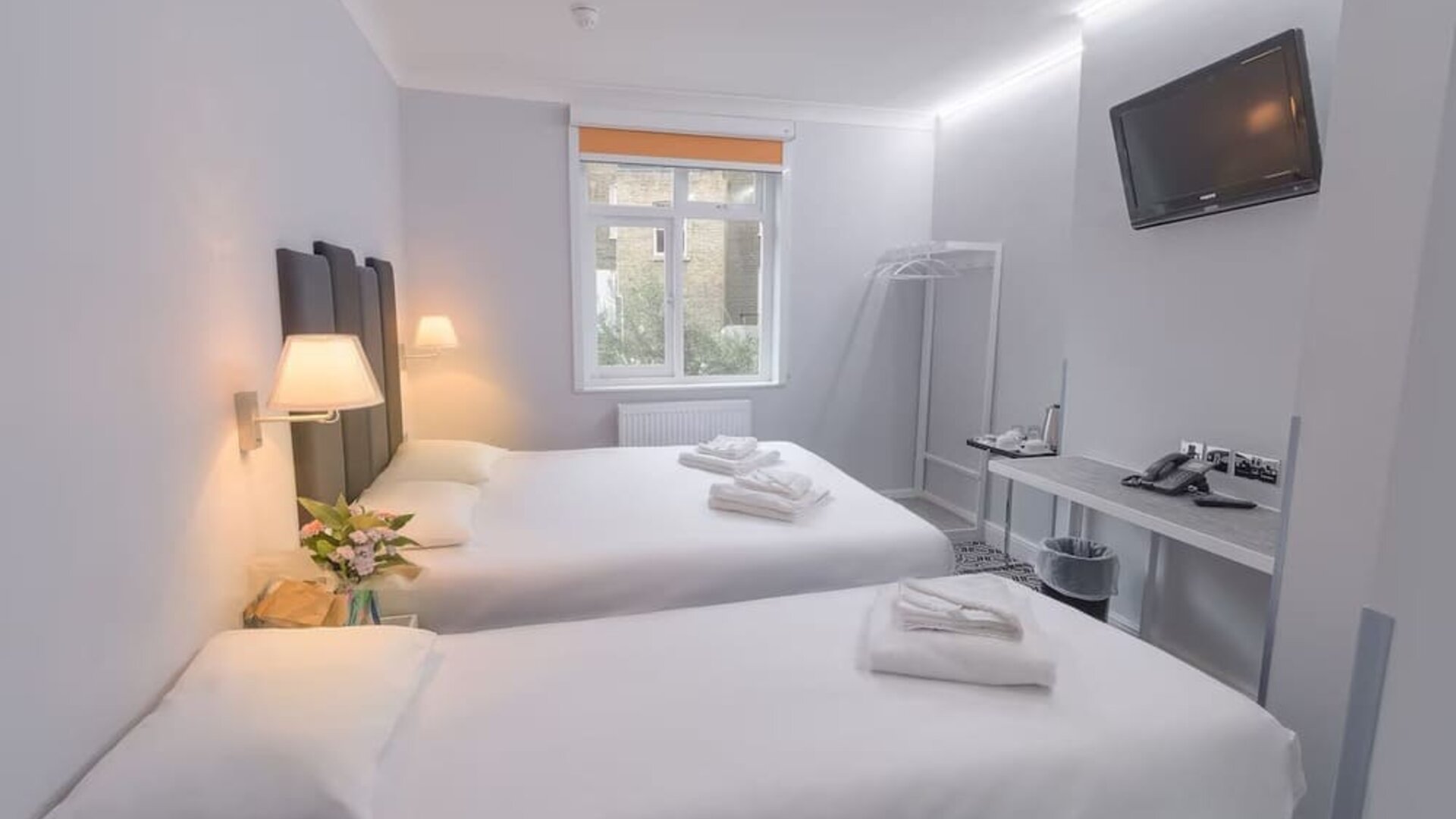 Double guest room with a white bed, dark upholstered headboard, bedside tables, wall-mounted reading lights and a large window at Victoria Inn.