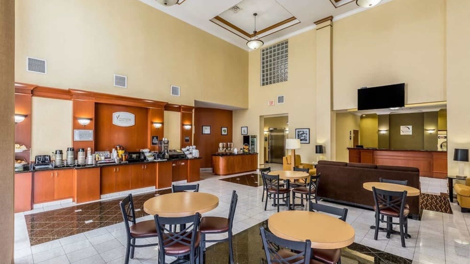 Hotel breakfast and lobby area with a coffee station, dining tables and chairs, reception desk, seating area, and polished tile floor at Sleep Inn & Suites Stafford - Sugar Land.