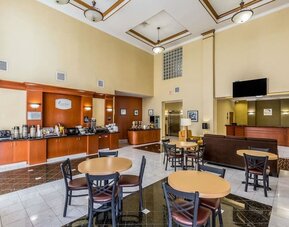 Hotel breakfast and lobby area with a coffee station, dining tables and chairs, reception desk, seating area, and polished tile floor at Sleep Inn & Suites Stafford - Sugar Land.