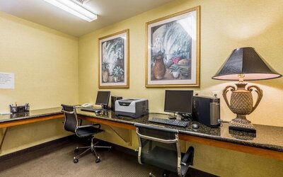Business center with two computer workstations, monitors, keyboards, office chairs, printer, and decorative artwork at Sleep Inn & Suites Stafford - Sugar Land.