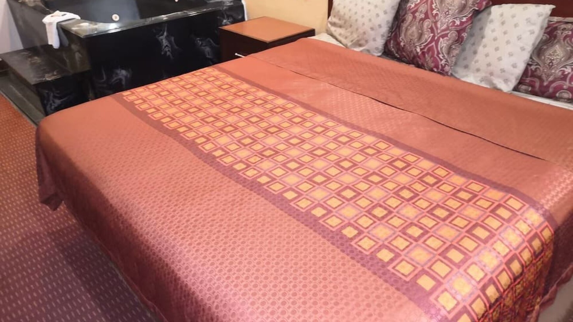 King guest room with a large bed featuring a red and gold patterned bedspread, dark wooden headboard, bedside tables, telephone, and black whirlpool tub beside the bed at Scottish Inn & Suites.