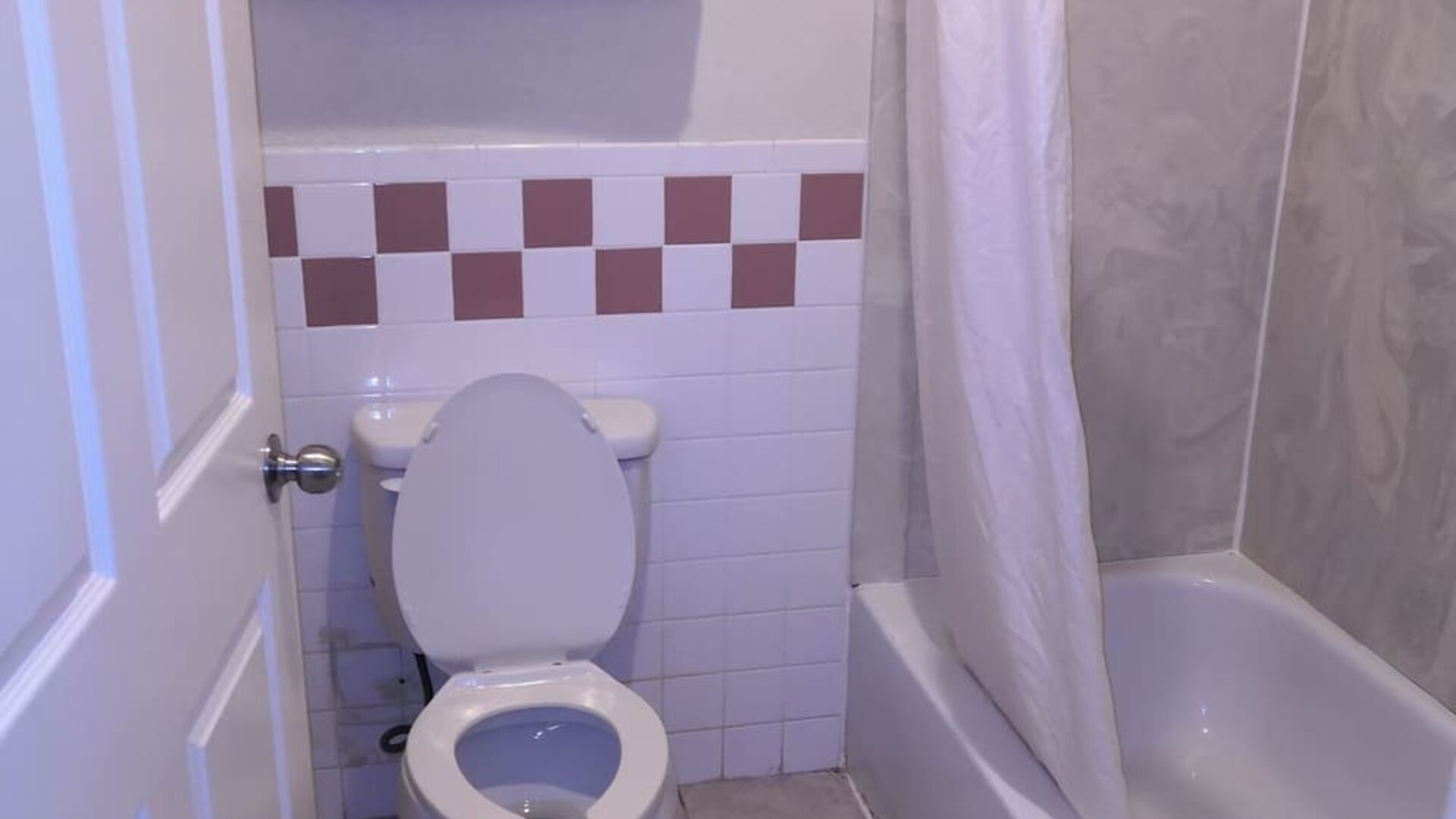 Bathroom with a bathtub and shower curtain, toilet, towel rack with folded towels, grab bar, and tiled walls at Scottish Inn & Suites.