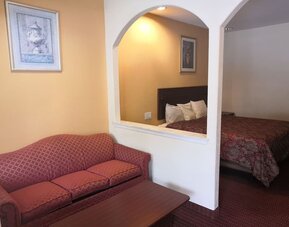 Guest room with a red patterned sofa and coffee table in the sitting area, with a king bed visible through two arched openings at Scottish Inn & Suites.