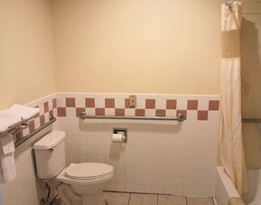 Accessible bathroom with a toilet, bathtub and shower, grab bars, towel racks, and tiled walls at Scottish Inn & Suites.
