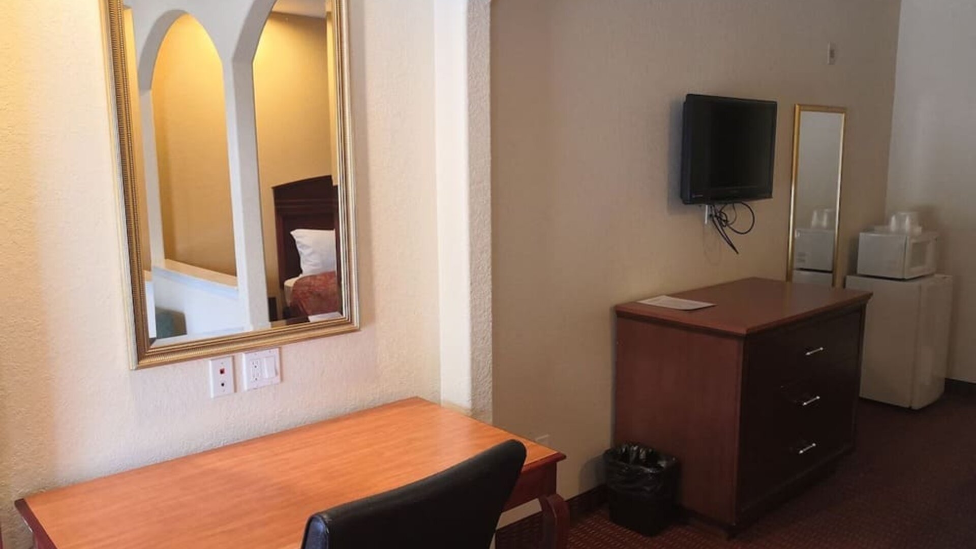 Guest room workspace with a wooden desk and chair, wall mirror, television, dresser, microwave, and mini refrigerator at Scottish Inn & Suites.
