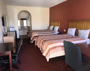 Guest room with two beds, striped orange and brown bedspreads, wooden headboards, desks and office chairs, television, and bathroom vanity visible through an arched opening at Scottish Inn & Suites.