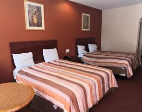 Guest room with two beds featuring striped orange, brown, and cream bedspreads, dark wooden headboards, bedside telephone, round table, and framed artwork at Scottish Inn & Suites.