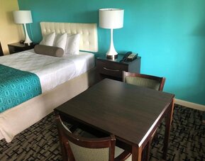 King guest room with a white tufted headboard, white bedding, turquoise patterned bed runner, dark bedside tables with lamps and telephone, and a dining table with chairs at Howard Johnson Express Inn - Rocky Hill.