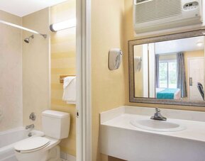 Bathroom with a bathtub and shower, toilet, white vanity with sink, large rectangular mirror, wall-mounted air-conditioning unit, and towel rack at Howard Johnson Express Inn - Rocky Hill.
