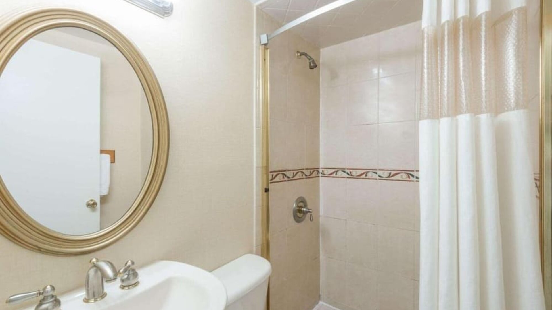 Bathroom with a glass-enclosed shower, white shower curtain, pedestal sink, oval wall mirror, and tiled shower walls at Howard Johnson Express Inn - Rocky Hill.