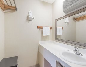 Bathroom vanity with a large rectangular mirror, white countertop and sink, towel rack with folded towels, wall-mounted hairdryer, and air-conditioning unit above the mirror at Howard Johnson Express Inn - Rocky Hill.