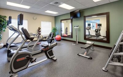 Hotel fitness center equipped with cardio machines, an exercise bench, free weights, medicine balls, a stability ball, large mirrors, and a wall-mounted television.
