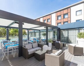 Outdoor terrace with lounge seating, dining tables, glass walls, and views of the hotel pool at Holiday Inn Toulouse Airport.