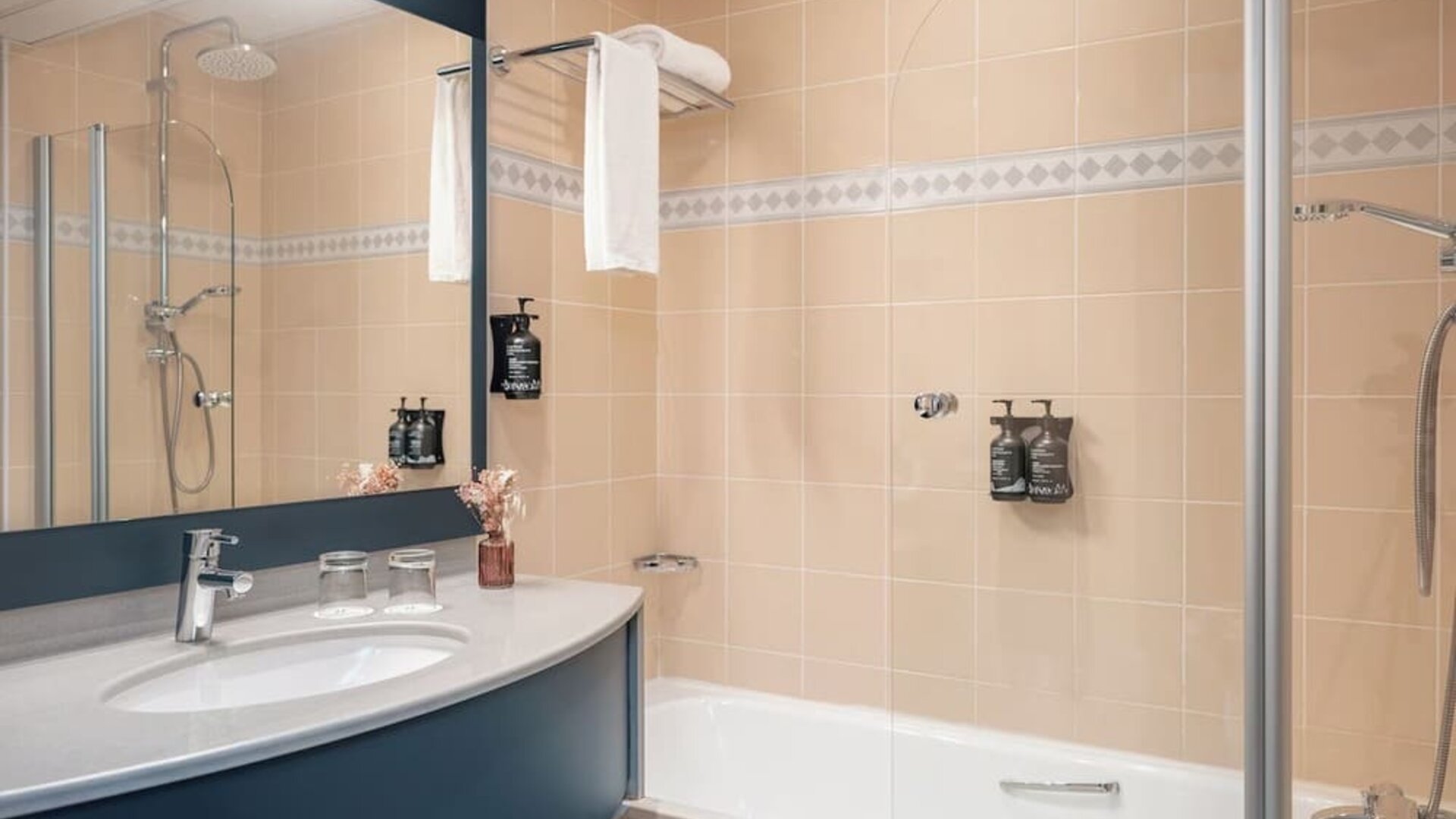 Bathroom with bathtub, glass shower screen, large mirror, vanity sink, toiletries, and towel rack at Holiday Inn Toulouse Airport.