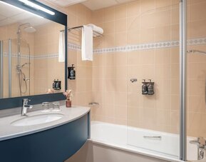 Bathroom with bathtub, glass shower screen, large mirror, vanity sink, toiletries, and towel rack at Holiday Inn Toulouse Airport.