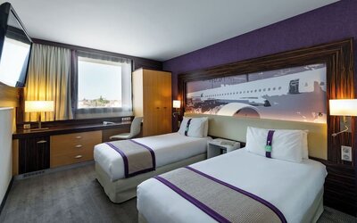 Guest room with two single beds, purple accents, airplane artwork, TV, work desk, and wardrobe at Holiday Inn Toulouse Airport.