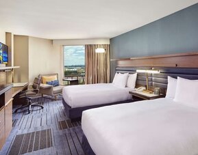 Guest room with two double beds, a blue accent wall, work desk, lounge chair, television, and large window at Hilton Newark Airport.