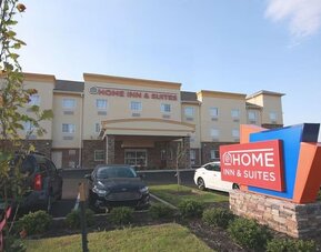 Exterior of At Home Inn & Suites showing the three-story hotel building, entrance, landscaped grounds, parking area, and hotel sign.