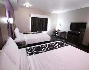 1. Guest room with two beds, white linens, black patterned bed runners, television, desk, dresser, and armchair at At Home Inn & Suites.