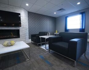 Hotel lounge seating area with black sofas, coffee tables, a fireplace, television, and large window at At Home Inn & Suites.