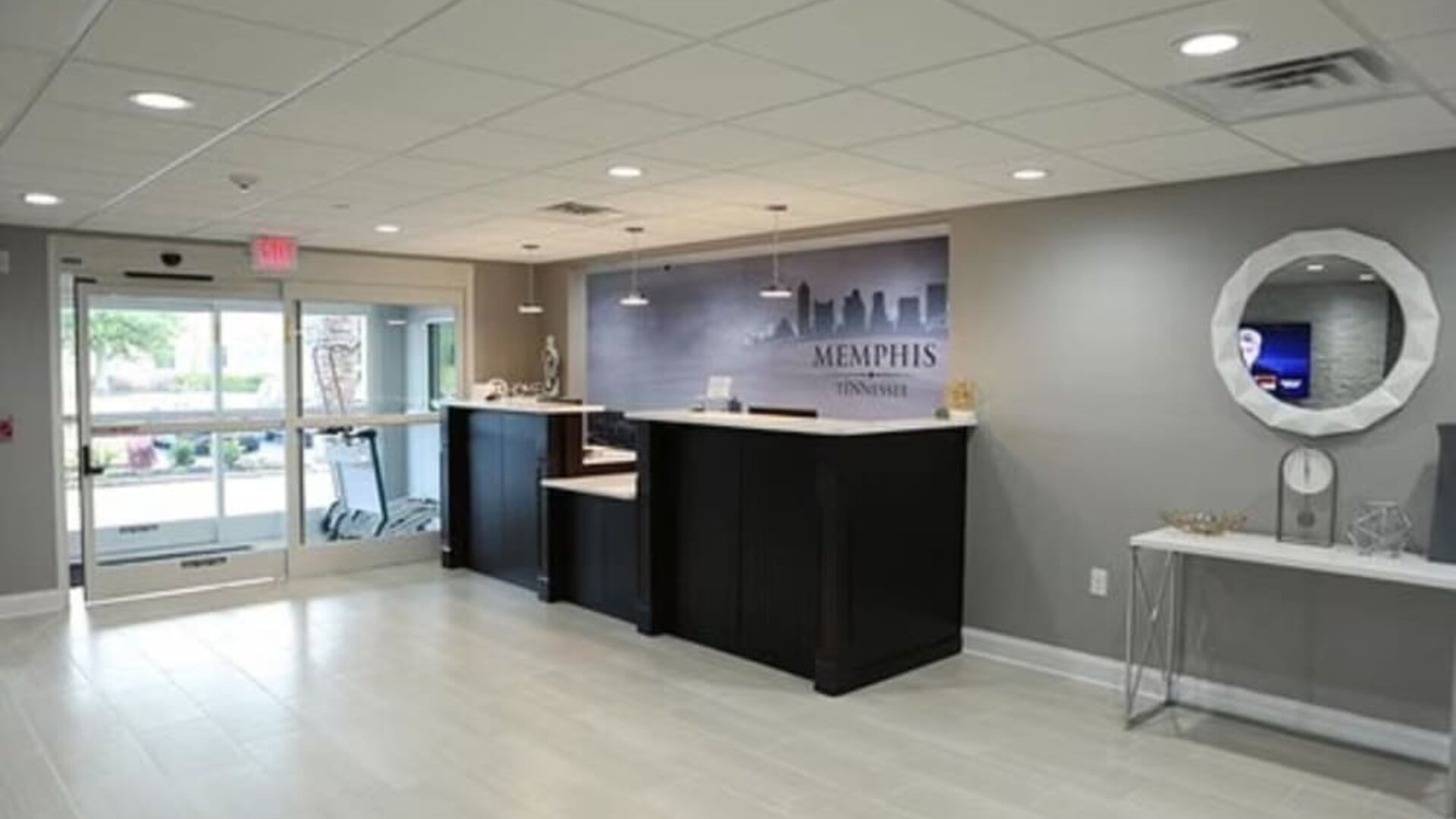 Hotel lobby with reception desks, entrance doors, decorative console table, and round wall mirror at At Home Inn & Suites.