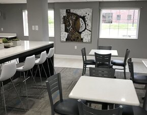 Hotel dining area with white tables, black chairs, bar-height seating, large windows, and contemporary artwork at At Home Inn & Suites.