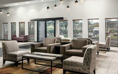 Spacious hotel lobby seating area with upholstered chairs and sofas, large windows, coffee tables, and contemporary decor at Garner by IHG.