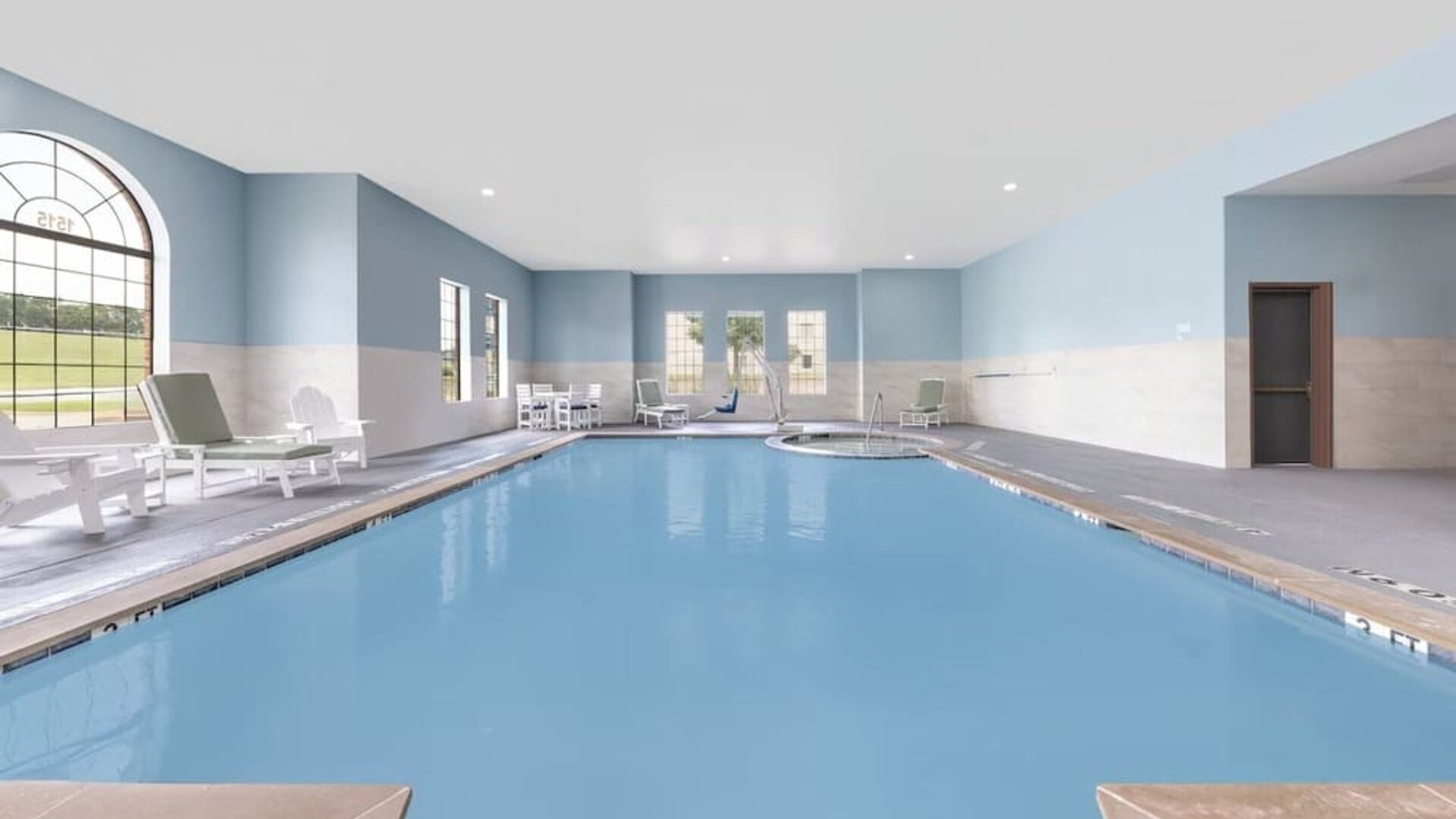 Indoor swimming pool with blue water, lounge chairs, large windows, and a separate whirlpool area at Holiday Inn Express & Suites Granbury.