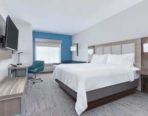 Bright guest room with a blue accent wall, large window, blue sofa, and king bed at Holiday Inn Express & Suites Granbury.