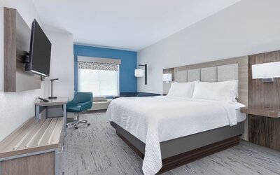 Bright guest room with a blue accent wall, large window, blue sofa, and king bed at Holiday Inn Express & Suites Granbury.