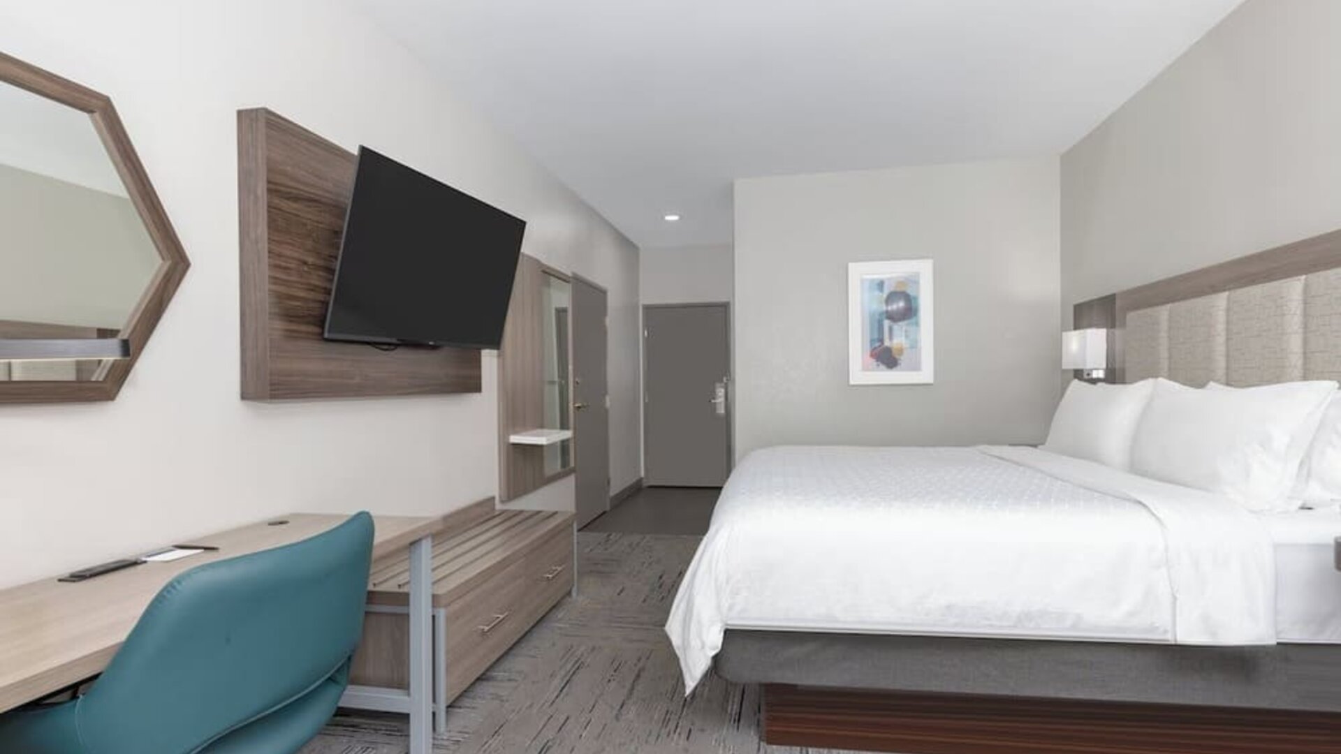 Spacious king guest room with a large bed, white bedding, wood furnishings, desk, blue office chair, and wall-mounted TV at Holiday Inn Express & Suites Granbury.