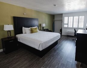 King guest room featuring a king bed, white bedding, green accent wall, bedside tables and lamps, desk, and large windows at Western Inn.
