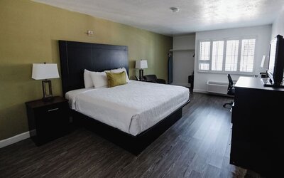 King guest room featuring a king bed, white bedding, green accent wall, bedside tables and lamps, desk, and large windows at Western Inn.