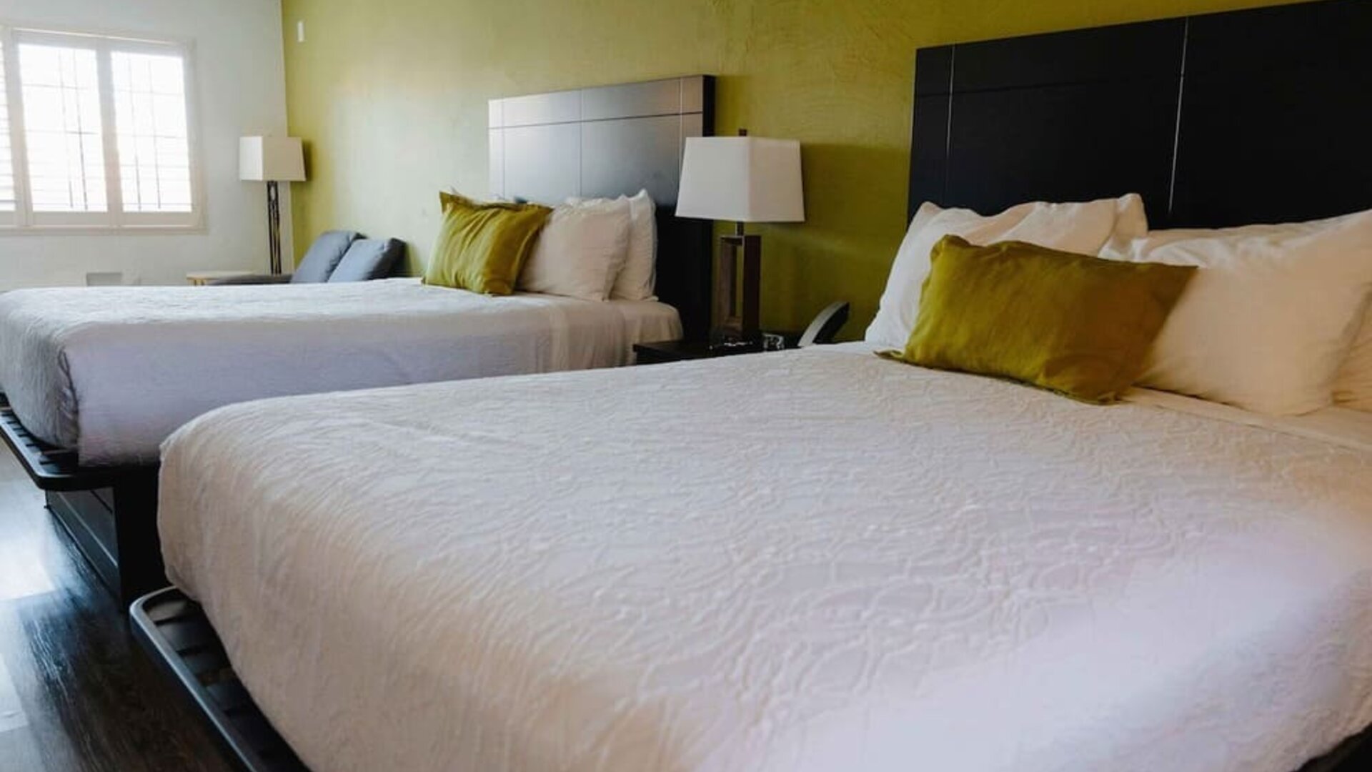 Guest room with two beds, white bedding, green accent wall, bedside lamps, and a window with natural light at Western Inn.Guest room with two beds, white bedding, green accent wall, bedside lamps, and a window with natural light at Western Inn.