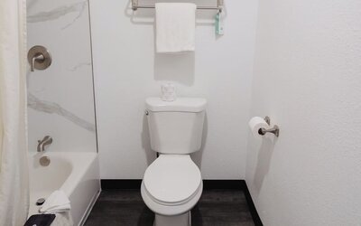 Bathroom with a bathtub/shower combination, white tile surround, towel rack, and toilet at Western Inn.
