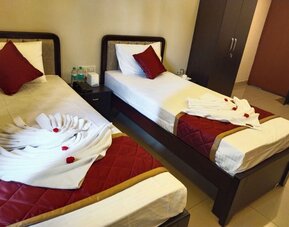 Twin bed guest room featuring white bedding, burgundy accent pillows, quilted runners, decorative folded towels with red flowers, and a bedside table with a telephone.