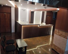 Modern hotel reception area featuring a dark wooden front desk with white countertops, decorative LED lighting, polished flooring, and guest seating.