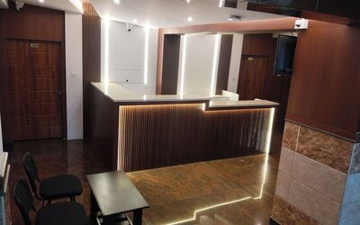 Modern hotel reception area featuring a dark wooden front desk with white countertops, decorative LED lighting, polished flooring, and guest seating.