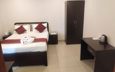 Bright double bed guest room featuring white bedding, burgundy accents, a wooden wardrobe, bedside cabinets, and a refreshment station with an electric kettle.