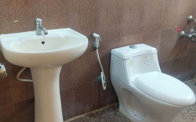 Private hotel bathroom featuring a white pedestal sink, modern toilet, handheld bidet sprayer, wall-mounted shower fixtures, large mirror, and patterned tile flooring.